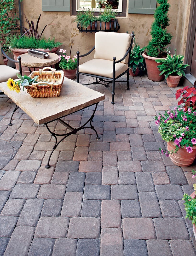 A DIY Stone Patio with a stone table, chairs, and plants on top of it.