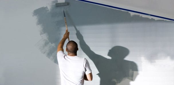 A man using a paint roller to paint a wall.