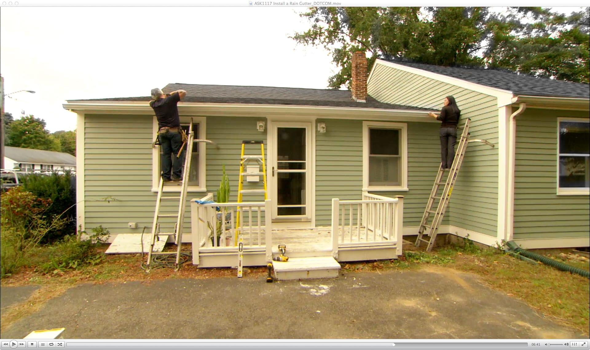 Two people on ladders installing a rain gutter system on a house.