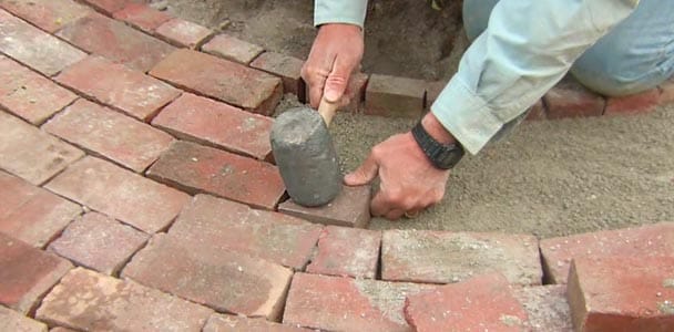 A man using a mallet to repair a brick walkway