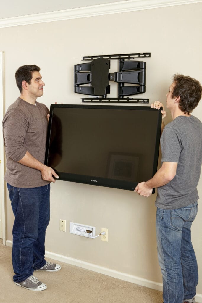 Two men lift ang hang a flat-screen TV on a TV wall mount.