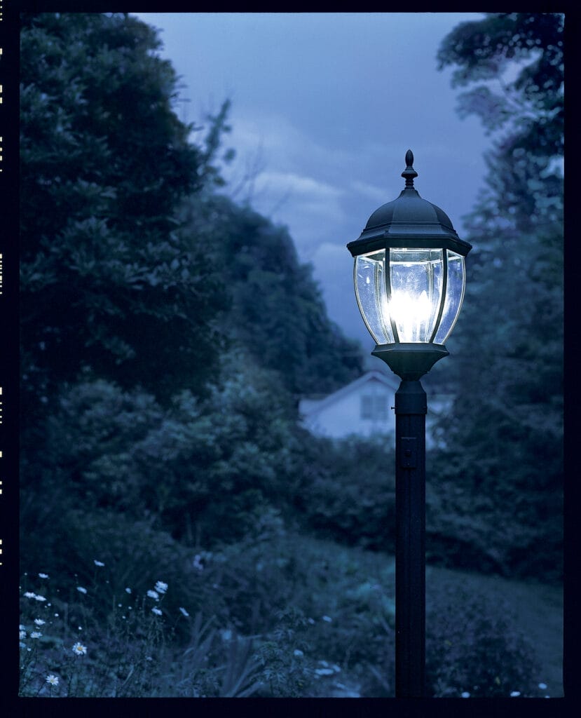 A lamppost installed in the grass shining on a dark night.