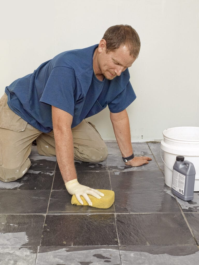 A person putting grout on a stone tile floor.