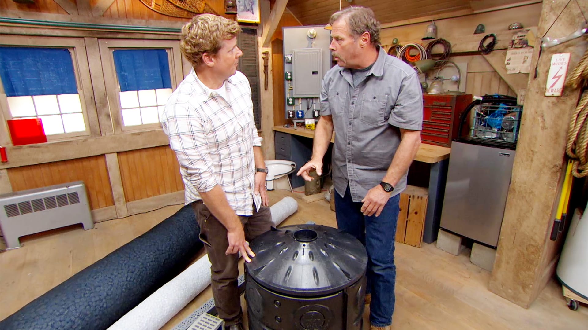 Two This Old House cast members discussing gutter drainage in a workshop.