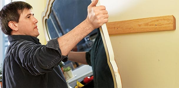 A person hangs a heavy mirror on the wall.