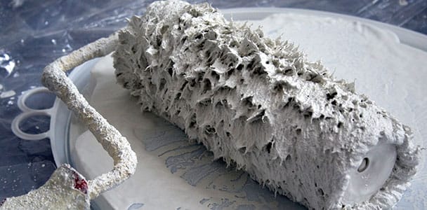A paint roller being rolled in white paint.
