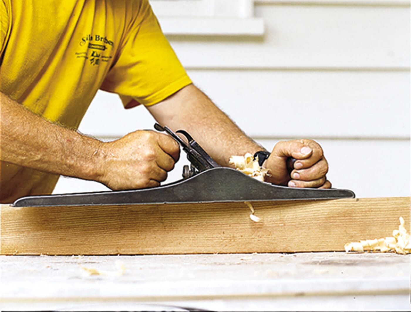 A man using a hand plane on a board of wood.