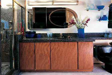 A bathroom with a black toilet and mirror over a black sinktop and brown cabinets