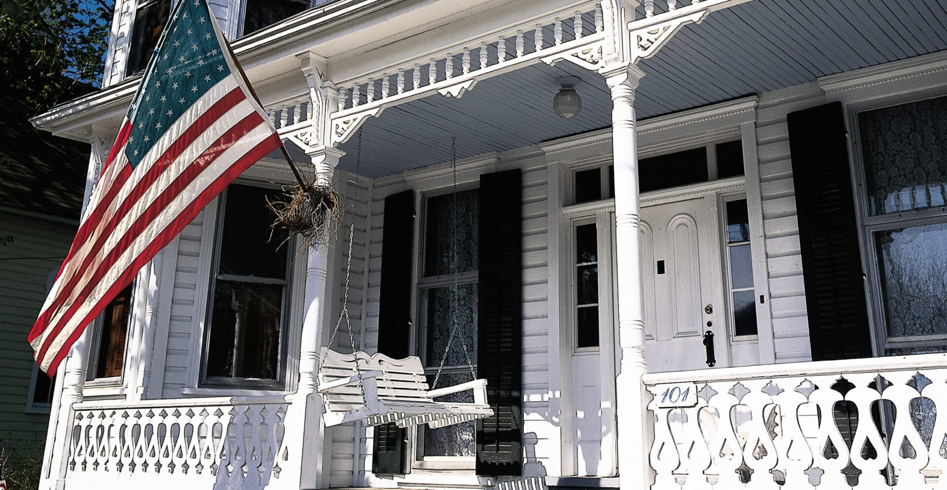 A white porch swing hanging below a large American flag.