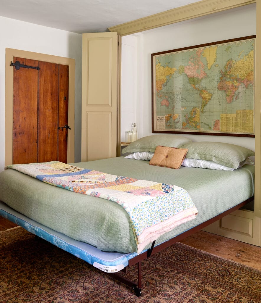 a murphy bed next to a door, it has a framed map above its head.