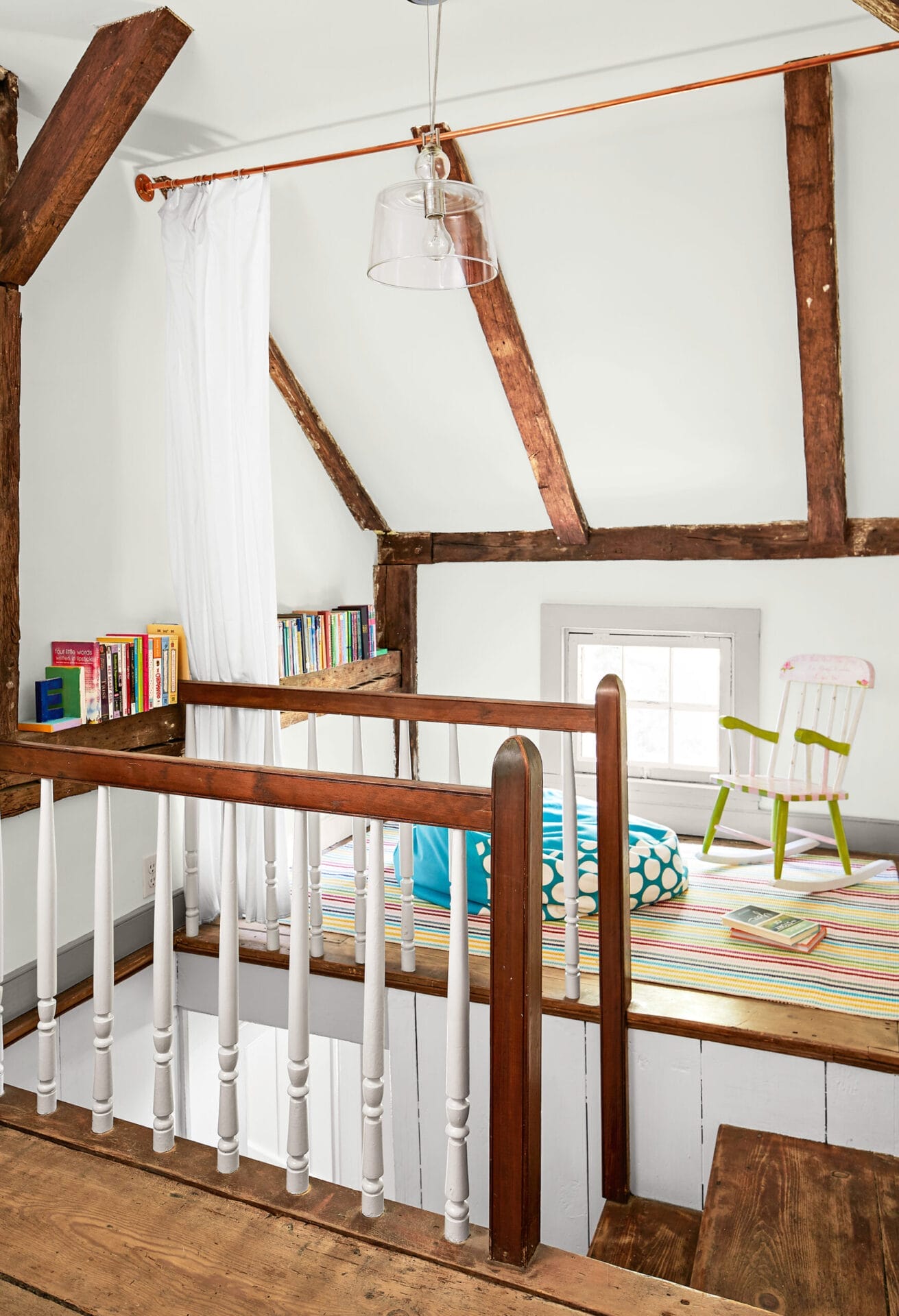 A nook at the top of a staircase with seating options and books.
