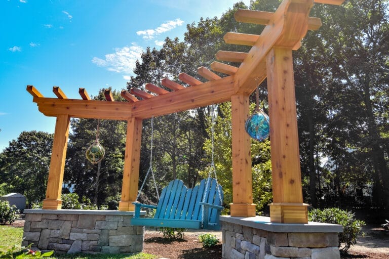 Angled cedar pergola with built-in Adirondack-style bench swing in backyard setting.