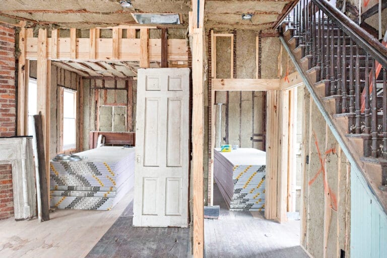 Interior view showing salvaged pine staircase, living room mantel, and pocket door in historic Charleston home.