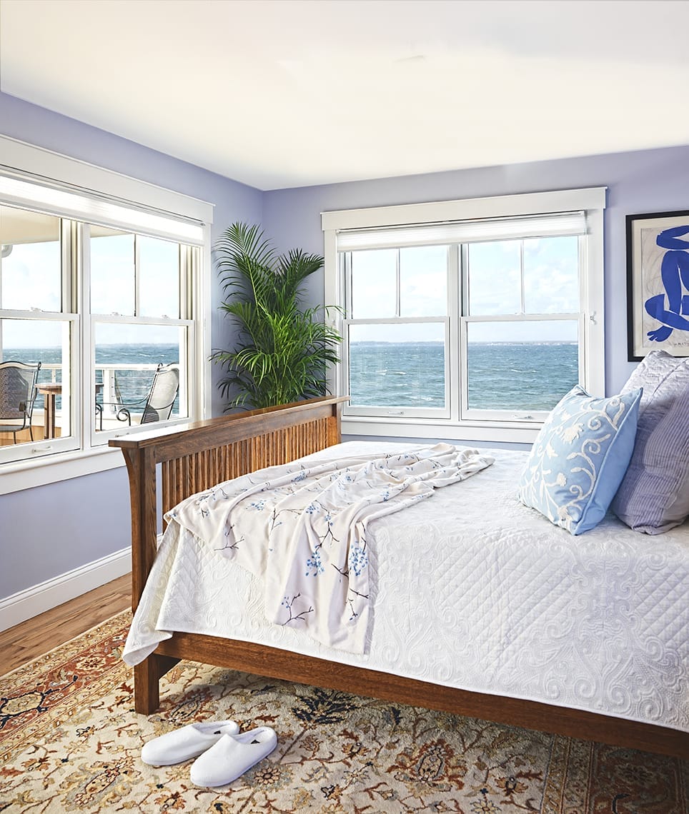 A bedroom overlooking the ocean with a light blue and purple colro scheme.