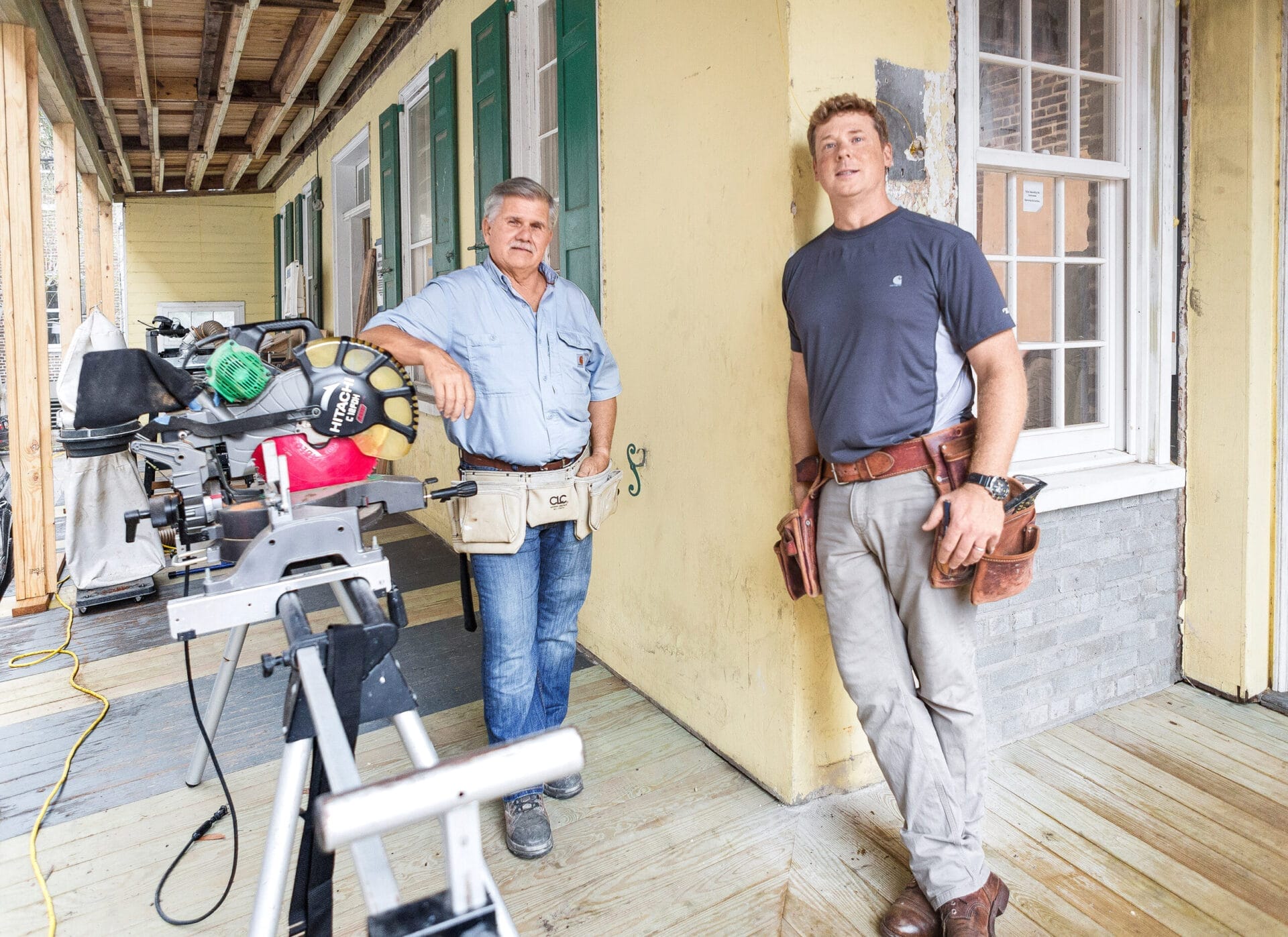 TOH general contractor Tom Silva and host Kevin O'Connor wearing tool aprons on first-floor piazza during renovation work.