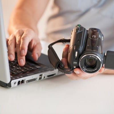 Someone holding a video camera and using a laptop