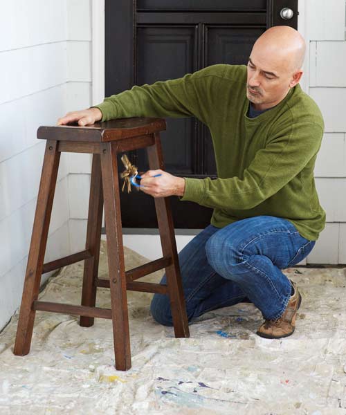 A man using a set of keys to distress a piece of furniture.
