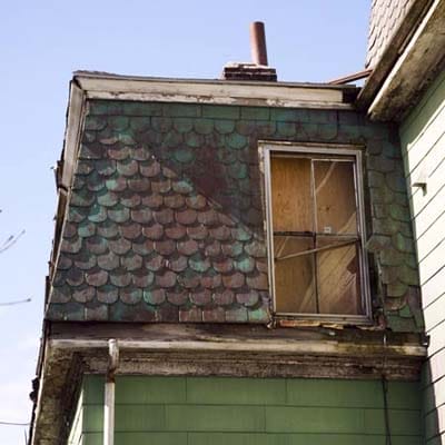 Deteriorating slate roof and green asbestos siding requiring replacement.