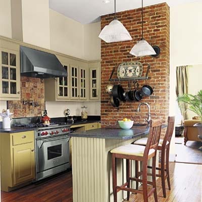 Kitchen with brick accent wall, two barstools, and green cabinets.