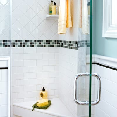 Corner shower with quartz seat, diamond-pattern tiles, glass mosaic band, and privacy window.
