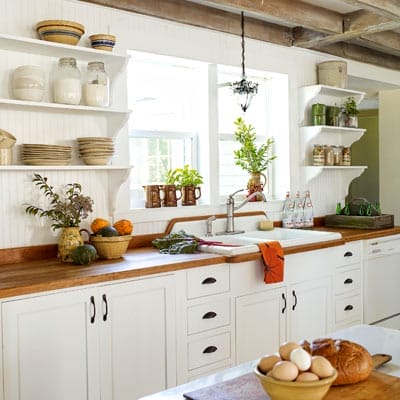 Bright farmhouse kitchen after renovation featuring white cabinets and open shelving.