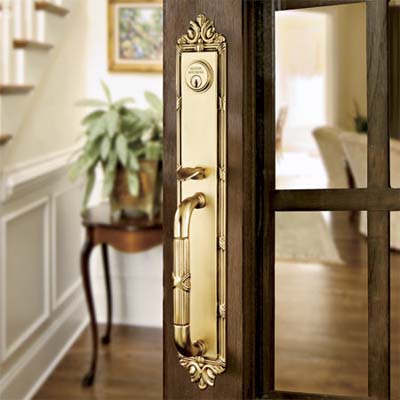 A polished brass entry set with intricate detailing installed on a dark wooden door.