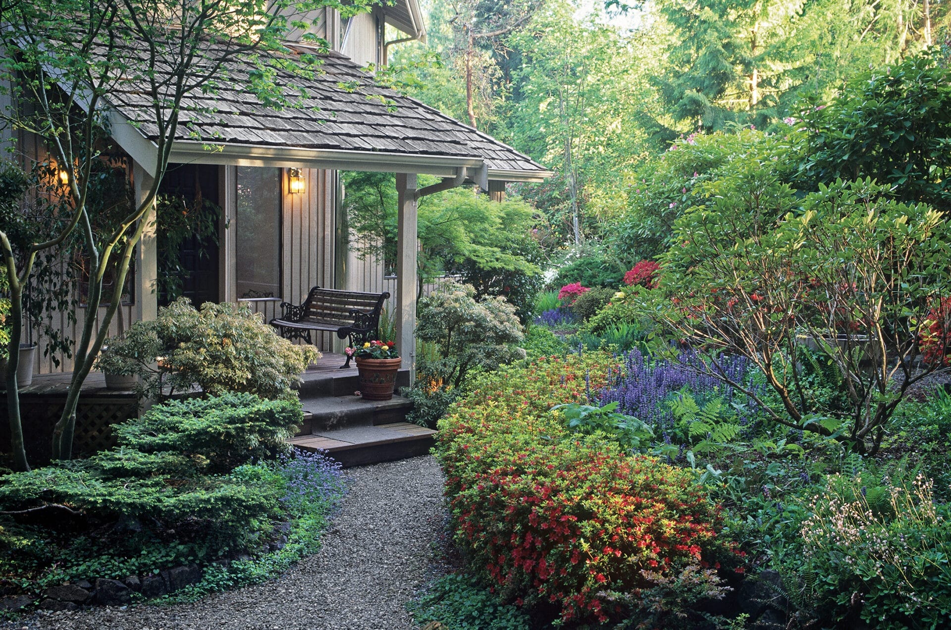Natural-looking landscape design with curved garden beds and scattered colorful flowers around home entrance.