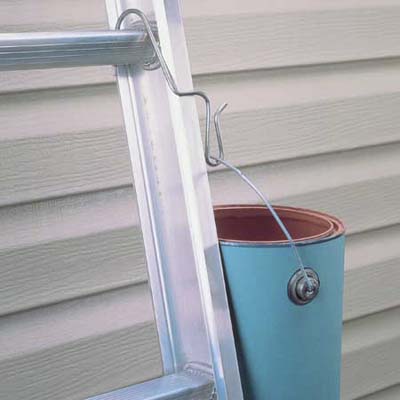 A silver ladder leaned against a building with a paint bucket hanging from its side.