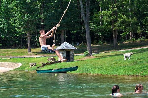A boy jumping off a rope swing into a pond.