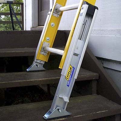 The base of a ladder with ladder levelers leaned against a building.