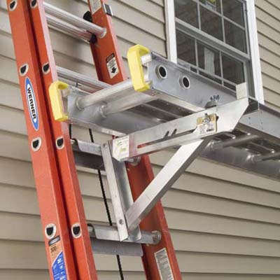A ladder leaned against a building with ladder jacks used to lift up another, horizontal ladder.