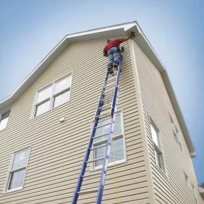 A man standing on a blue ladder working on the side of a building.
