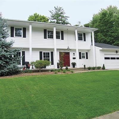 Plain white 1968 neo-colonial house with tall thin columns supporting long front porch.