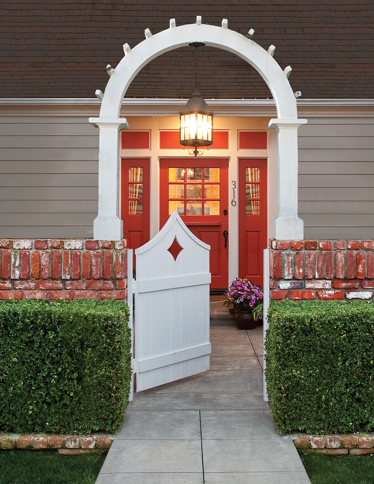 Brick courtyard entrance with white wooden gate, archway and red front door with sidelights.