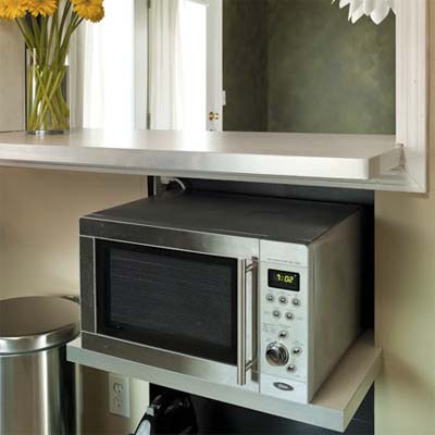 Under-counter storage shelves holding microwave beneath breakfast bar area.