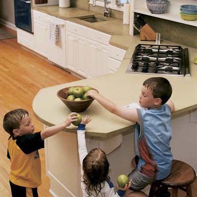 Three children taking fruit from a bowl on a concrete countertop.