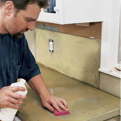 A man using a sponge to clean a concrete countertop.