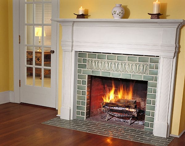 A tiled fireplace in front of a yellow wall in a home.