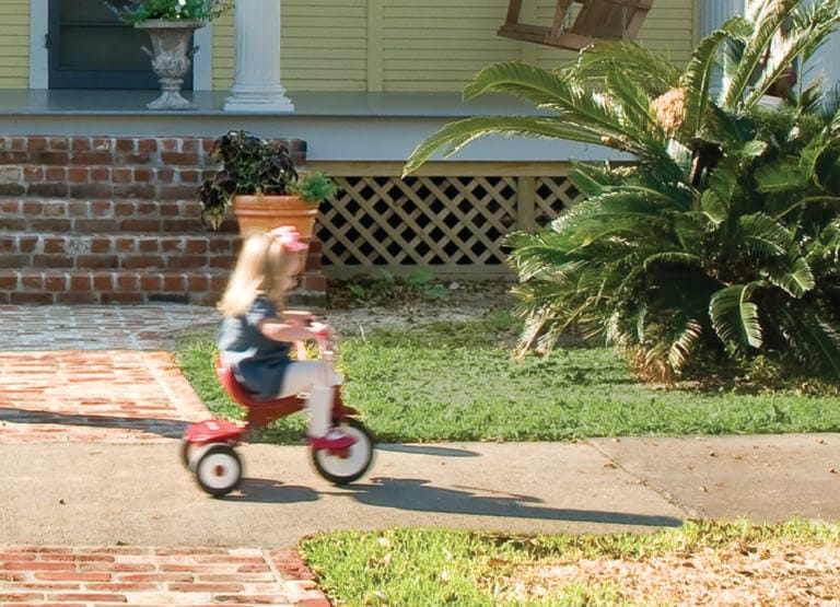 Little girl riding a tricycle in front of porch lattice.