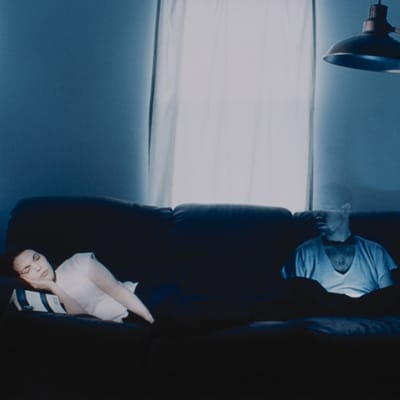 A woman sleeping on a couch next to a ghostly man.