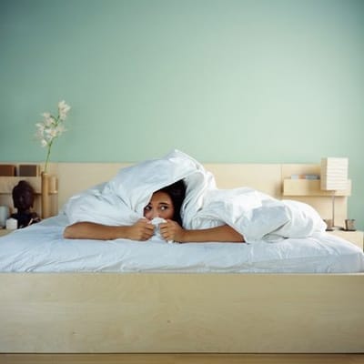 A woman hiding under the covers of her bed.