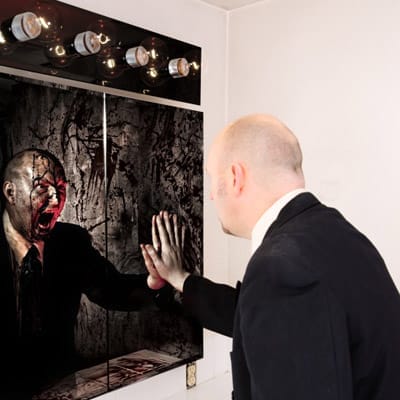 A man looking in the mirror and seeing a haunted visage of himself in it.