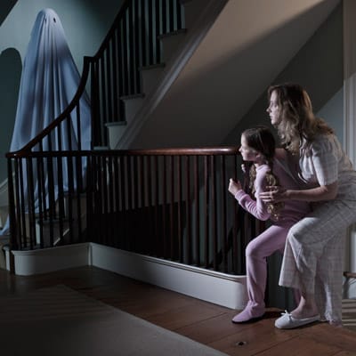 Two people cowering behind the stairs from a ghost.
