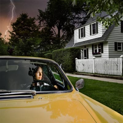 A woman in front of a house with a lightning strike in the background.
