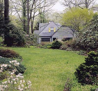 View of garden with oak and maple trees near a house.