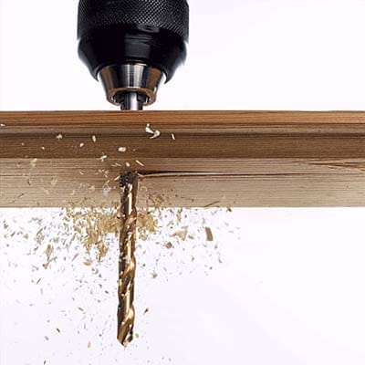 A drill bit pushing through a board of wood.