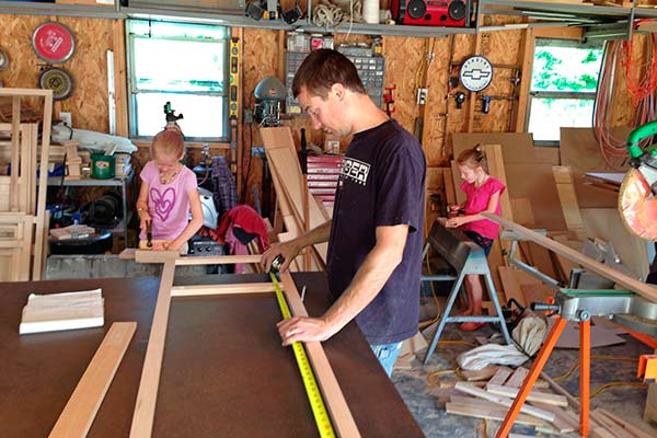 Husband building white kitchen cabinets with children helping in construction.
