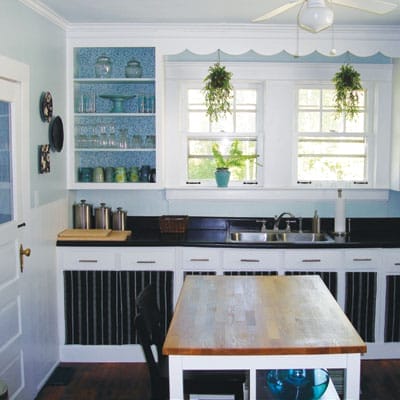 Butcher block island cart in cheerful renovated kitchen with exposed shelving.