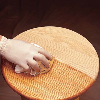 Gloved hand applying polyurethane to a wooden side table.