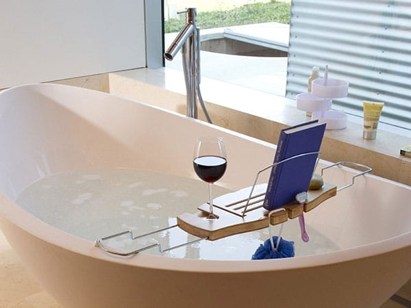 A bathtub caddy holding a book and a glass of wine.